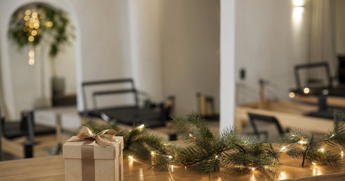 A small wrapped gift box with a ribbon sitting on the reception counter of a pilates studio decorated with a few pine branches and warm string lights, no text visible